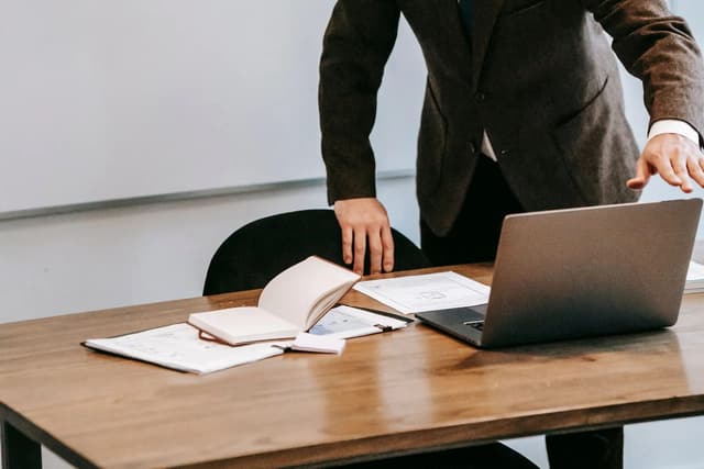 A man standing beside an open laptop and a notebook on a desk