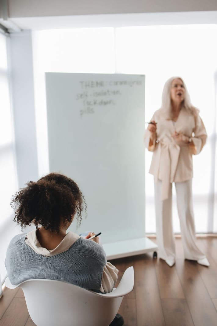 A seated student listening to an instructor beside a whiteboard